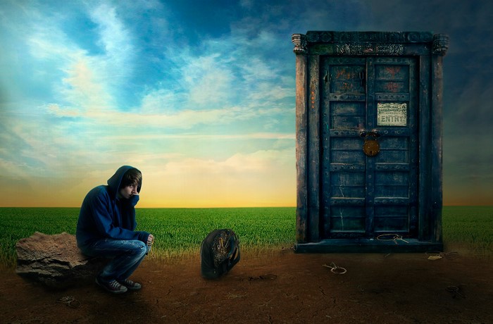 Boy in hoodie sitting by a mysterious door