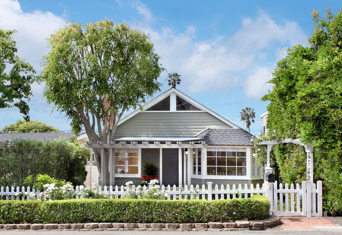 Green house with white picket fence and trees