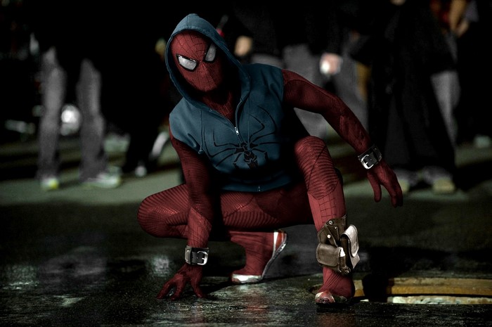 Spider-Man in a blue hoodie crouches on wet ground