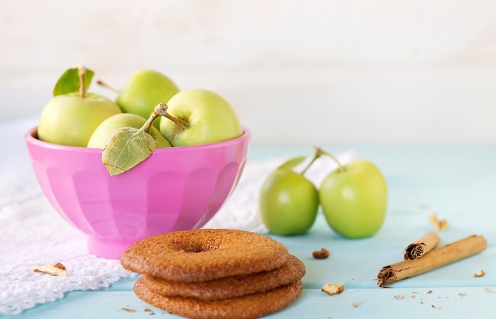 Green apples in a pink bowl with cookies and cinnamon sticks
