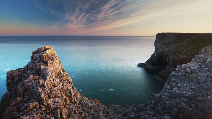 Rocky cliffs overlooking a calm sea at sunset