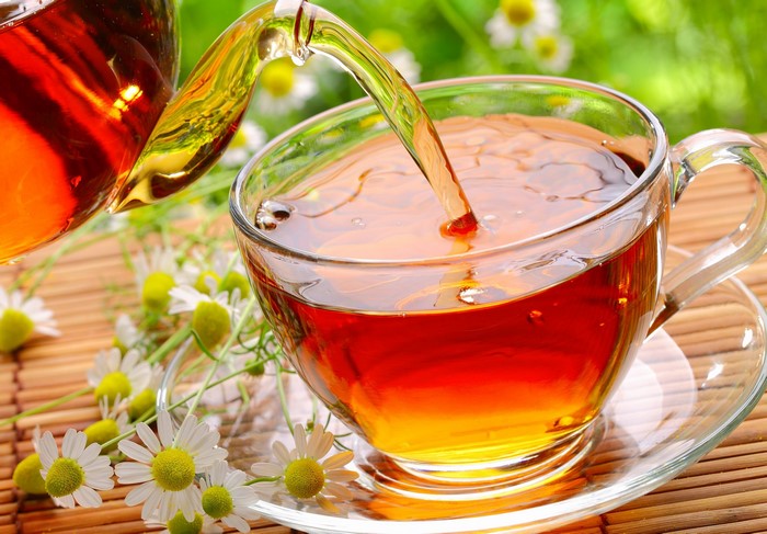 Tea being poured into a cup with chamomile flowers