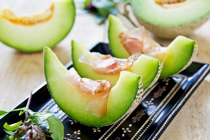 Cantaloupe slices with prosciutto on a black platter