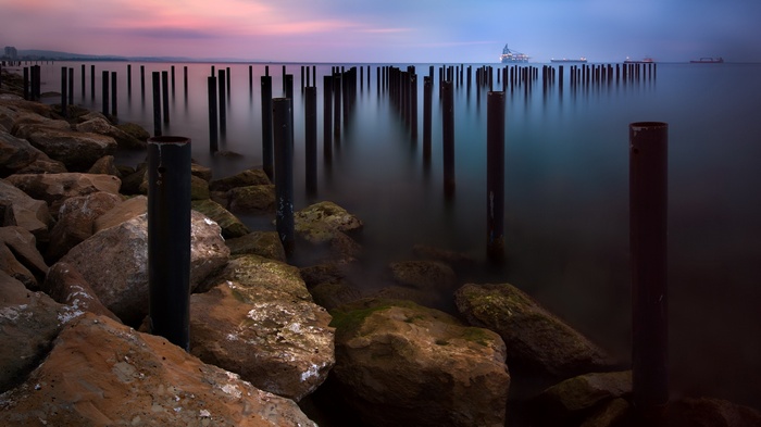 Ocean pier pilings at twilight with ships in distance