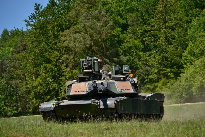 M1A2 Abrams tank in a grassy field with trees