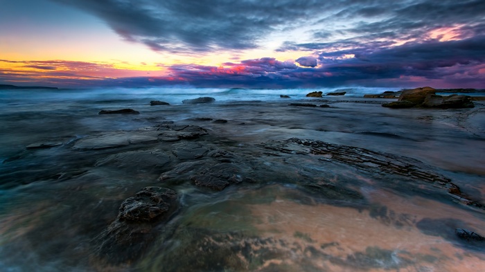 Ocean waves crashing on rocky shore at sunset