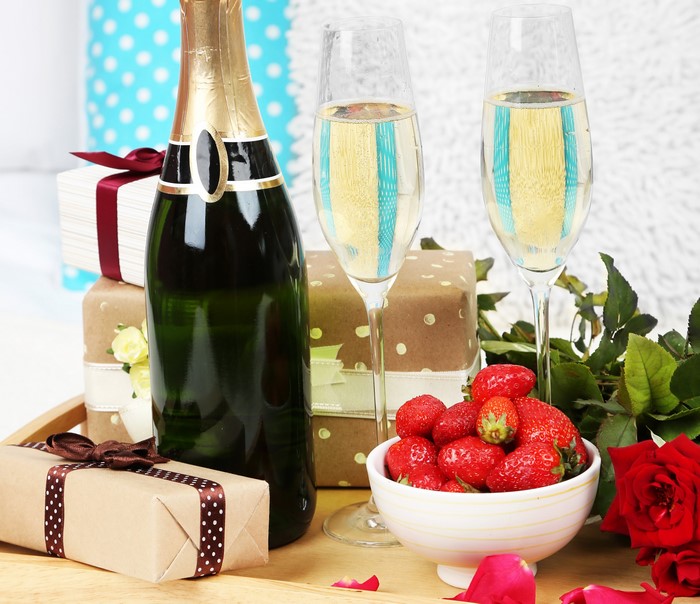 Champagne bottle, glasses, strawberries, and gifts on a tray