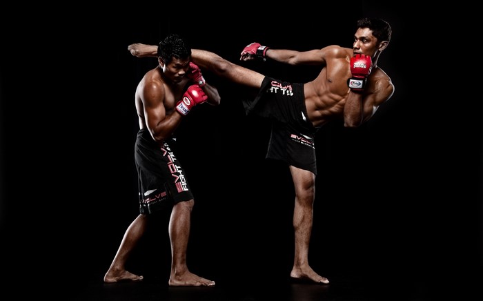 Two men in Muay Thai shorts and gloves fighting