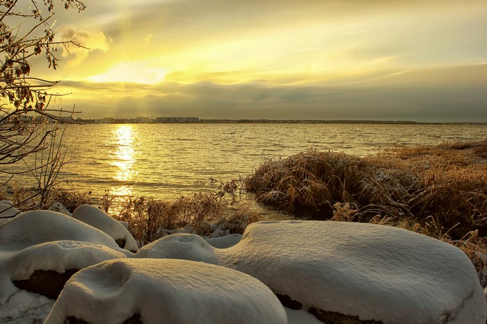Winter sunset over a calm sea with snow-covered rocks