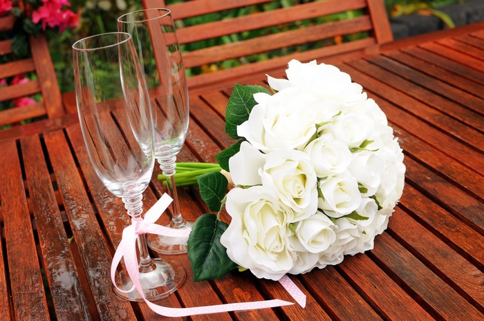 Two champagne glasses and a bouquet of white roses on a wooden table