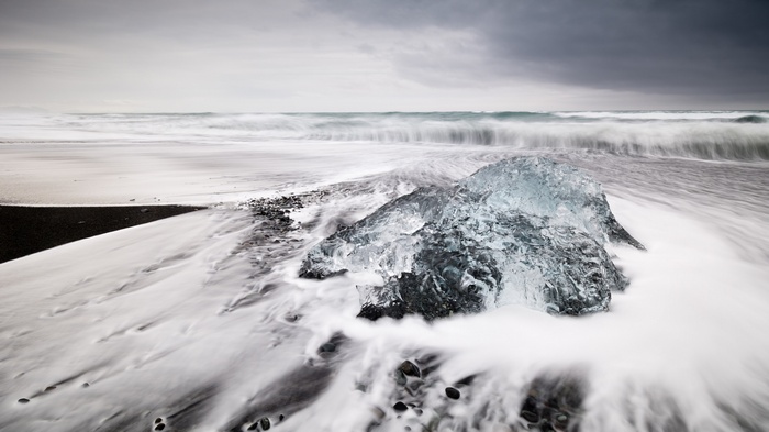 Iceberg on a black sand beach with waves
