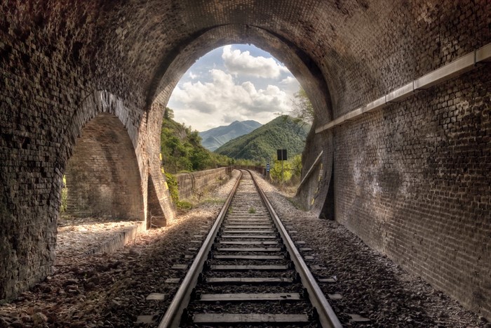 Train tracks through a brick tunnel to mountains