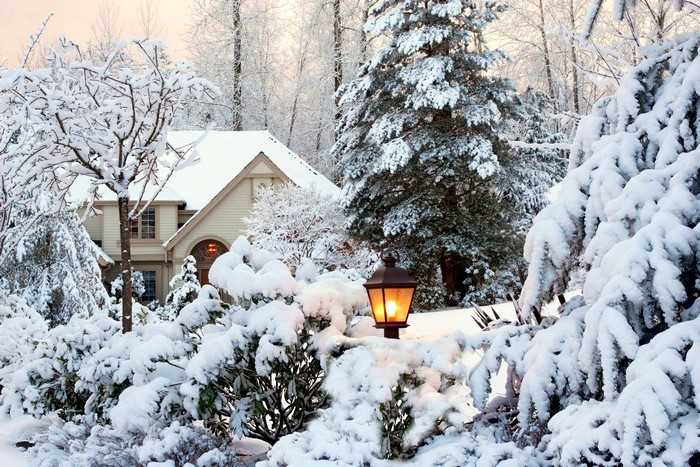 House covered in snow with a lit lantern