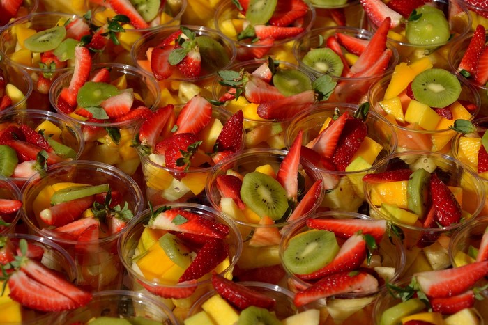 Many cups of fruit salad with strawberries, kiwi, and mango