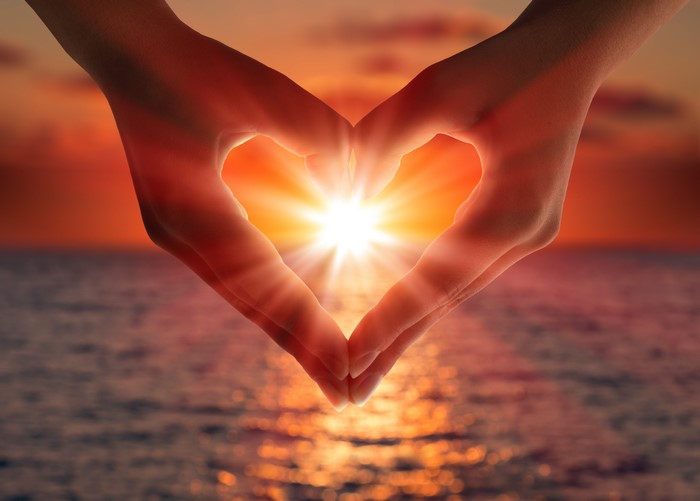 Hands forming a heart shape at sunset over the ocean