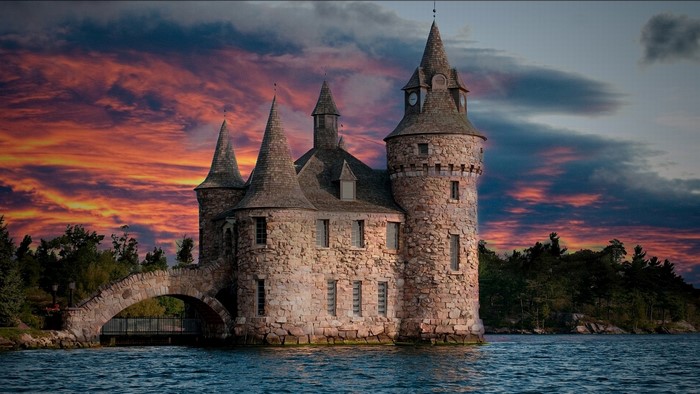 Castle on the water with a stone bridge and sunset sky