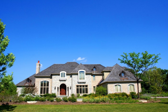 Large stone mansion with manicured lawn and trees