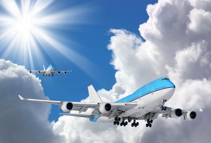 Two airplanes flying in the sky with sun and clouds