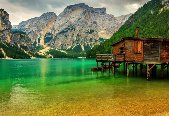 Wooden cabin on stilts by a turquoise lake with mountains