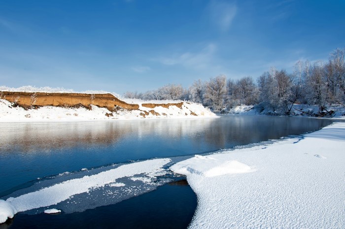 Winter riverbank with snow and ice under a blue sky