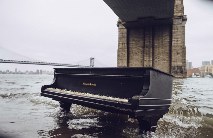 Piano submerged in water under a bridge
