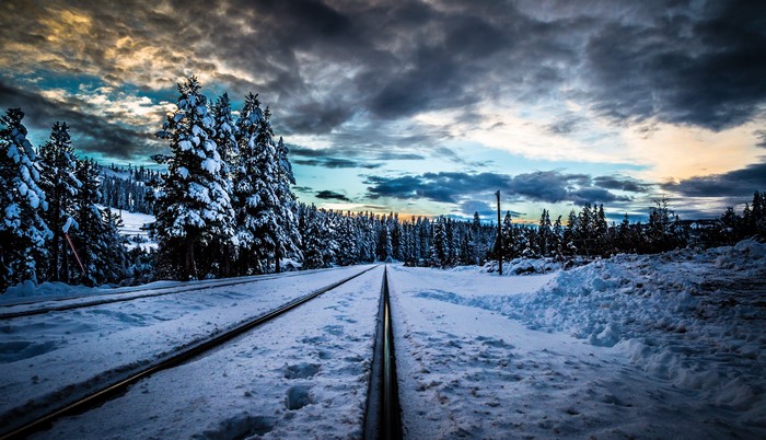 Railroad tracks in a snowy forest under dramatic clouds
