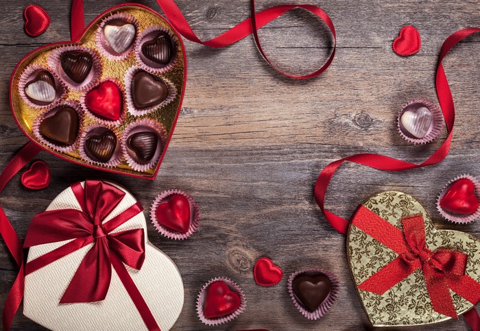 Heart-shaped chocolate boxes and red ribbons on wooden background