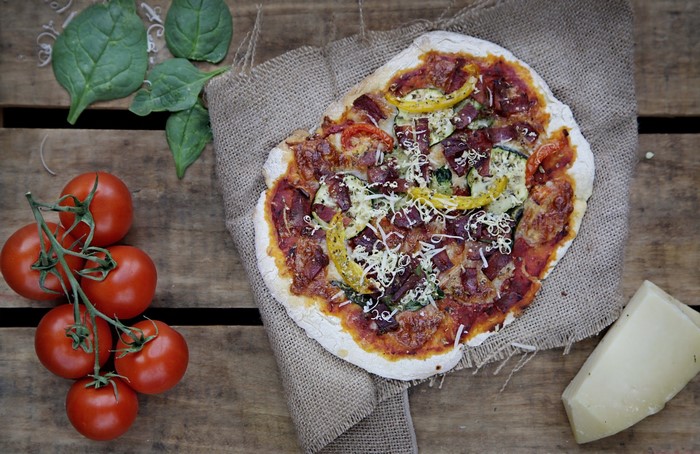 Pizza with tomatoes and spinach on a wooden table
