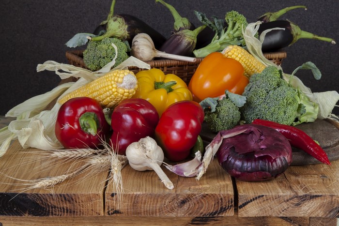 Still life of fresh vegetables including bell peppers, corn, garlic, and eggplant