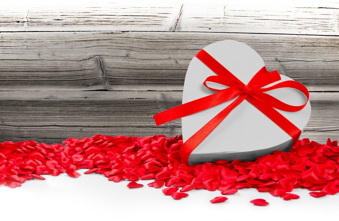 Heart-shaped gift box with red ribbon and petals