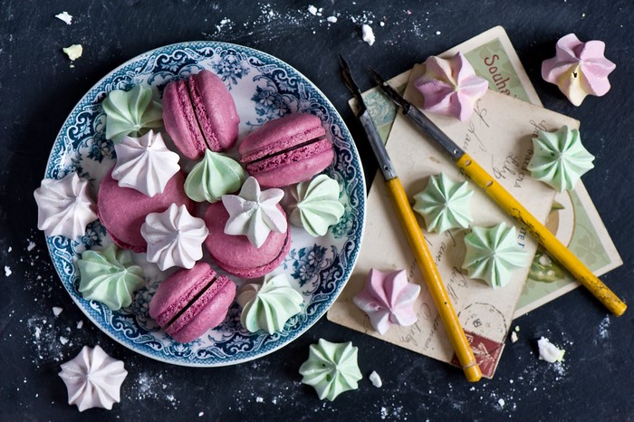 Pink macarons and meringues on a plate with vintage postcards