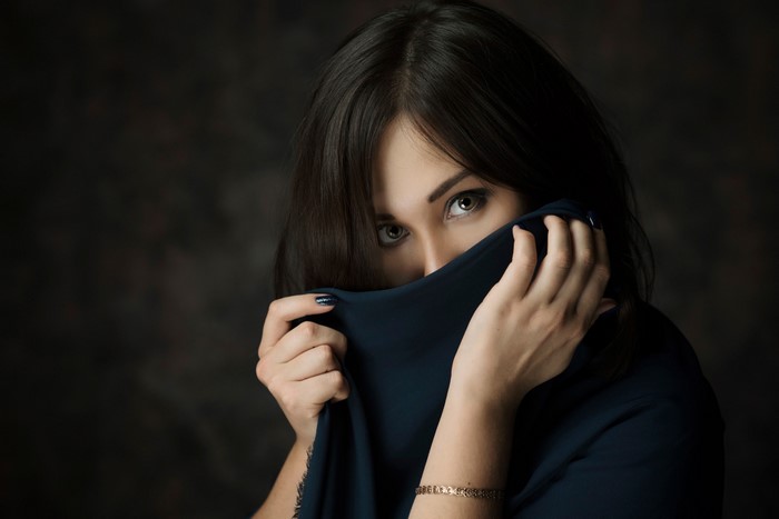 Brunette girl hiding face with dark fabric