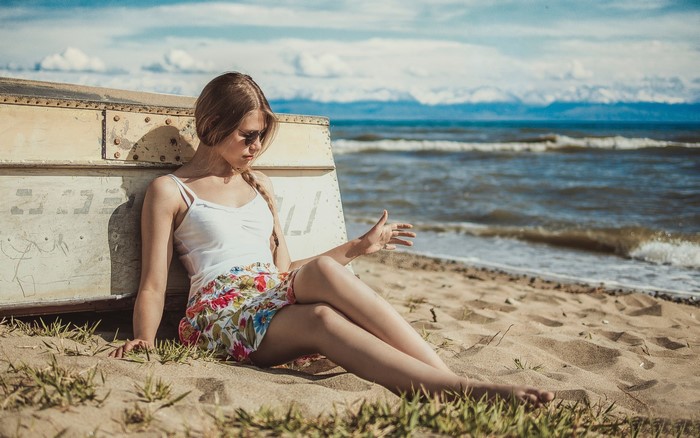 Girl in floral skirt sitting by boat on beach
