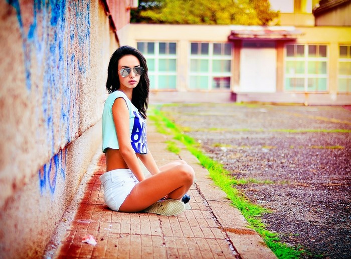 Brunette girl wearing sunglasses and crop top sitting by graffiti wall