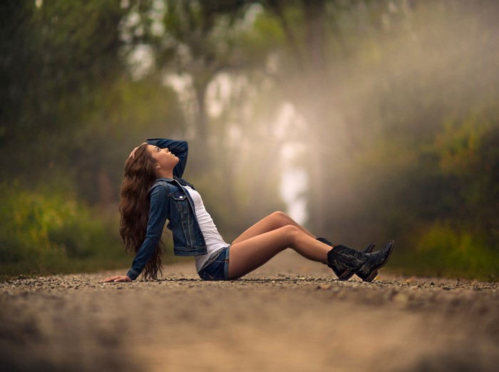 Woman in denim jacket and shorts sitting on a road