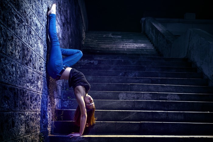Woman doing a handstand on a wall next to stairs