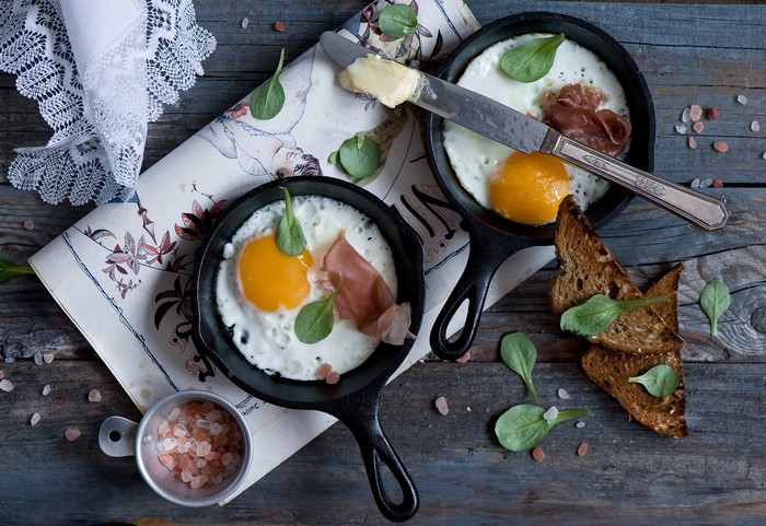 Fried eggs with prosciutto and toast in cast iron pans