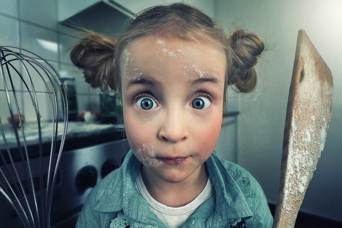 Girl covered in flour holding a spatula
