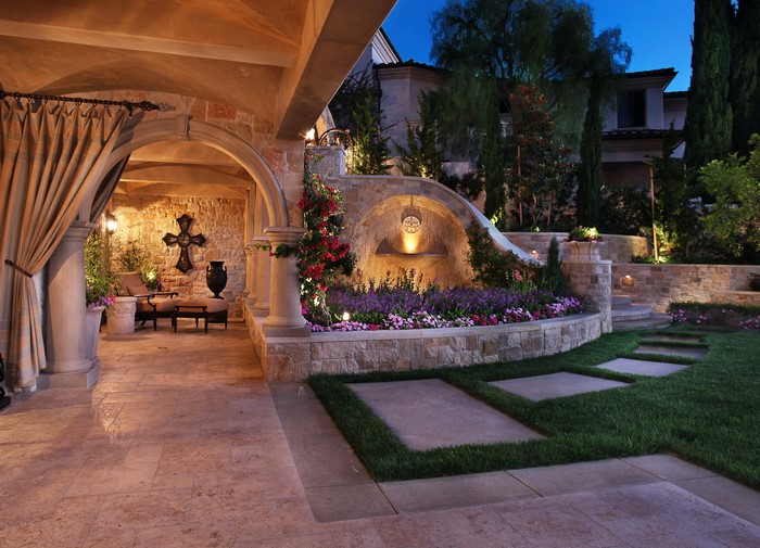 Outdoor patio with stone fountain and landscaping at night
