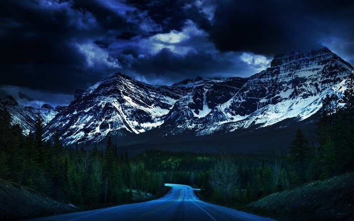 Road leading to snow-capped mountains under dark clouds