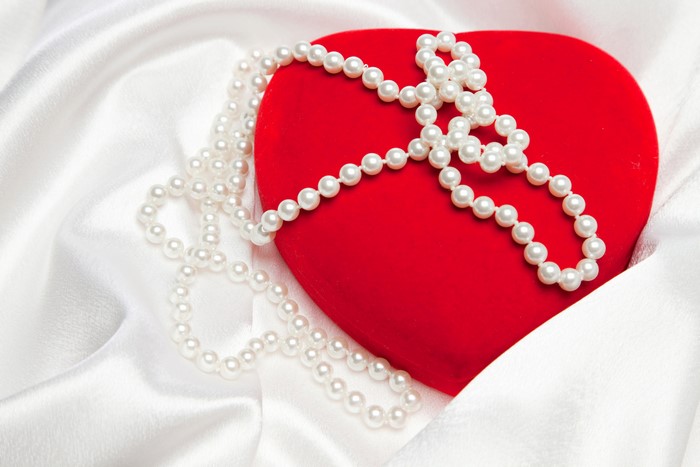 Red heart box with pearl necklace on white satin