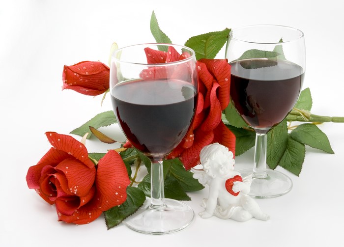 Two glasses of red wine with red roses and an angel figurine