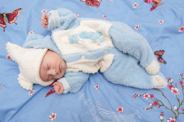 Baby in blue outfit and winter hat sleeping