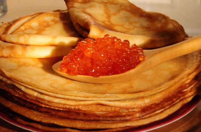 Pancakes with red caviar on a wooden spoon