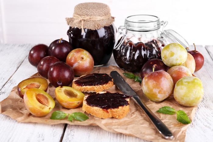 Plum jam in jars with plums and toast on a wooden table