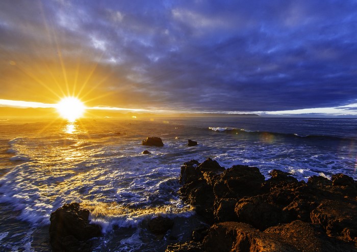 Sunset over the ocean with rocks and clouds