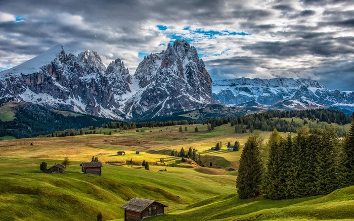 Snow-capped mountains over green grasslands with houses in Italy