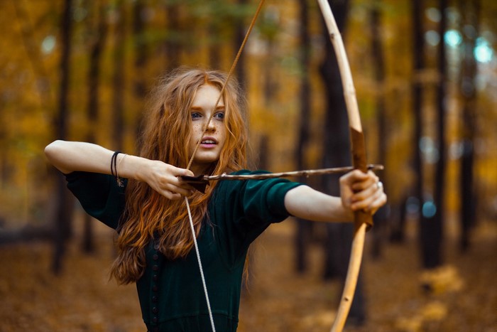 Redhead girl with bow and arrow in forest