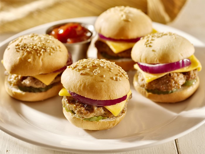Four mini cheeseburgers with red onion and ketchup