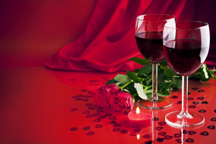 Two glasses of red wine with roses and a candle